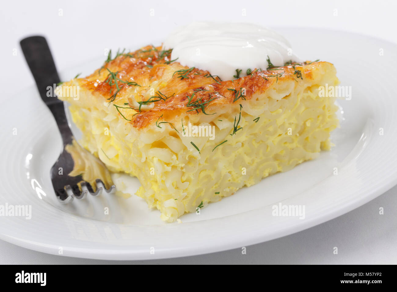 Gratin with pasta, beaten eggs, and cheese, plated with dill and sour cream Stock Photo
