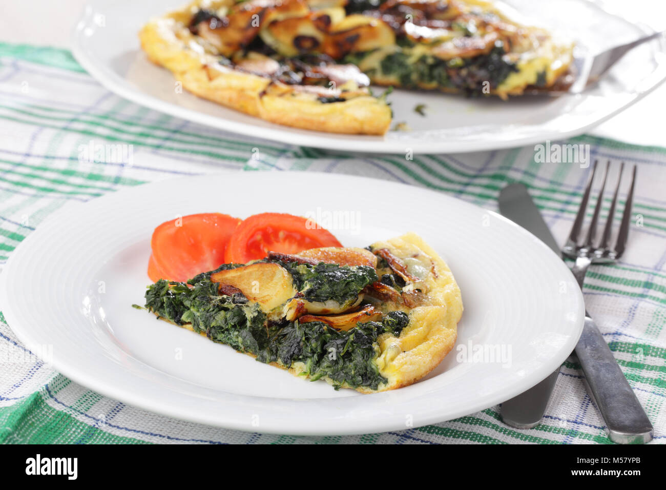 Frittata with spinach, potato, and tomato on white plate Stock Photo