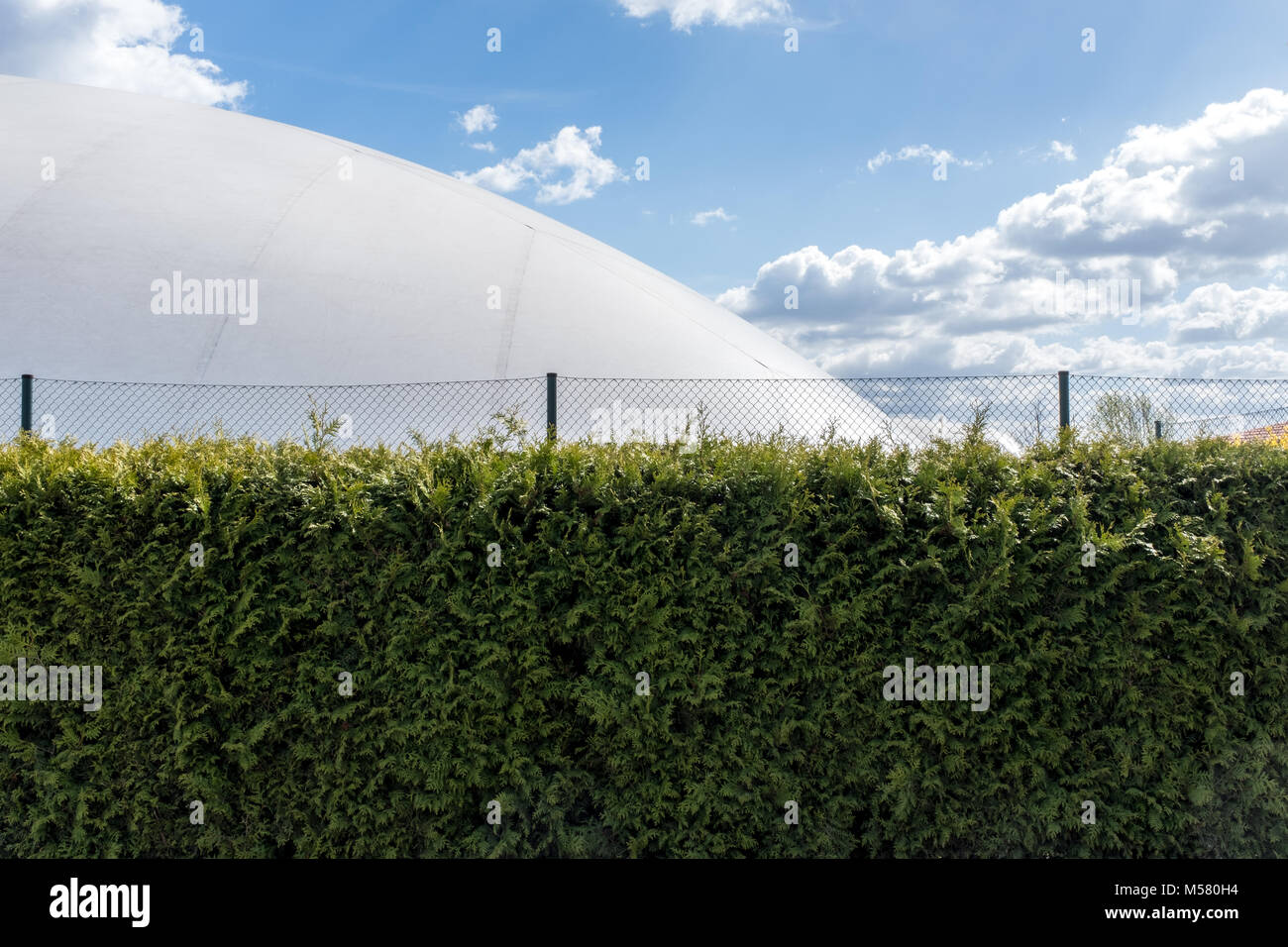 Inflatable tennis hall behind a fence and a hedge, bue sky with some clouds in the background. Stock Photo