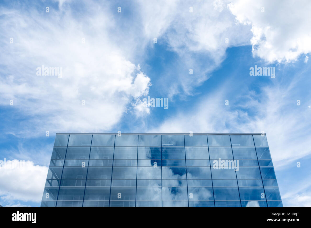 Office building against the blue, cloudy sky, mirroring in the glass front. Stock Photo