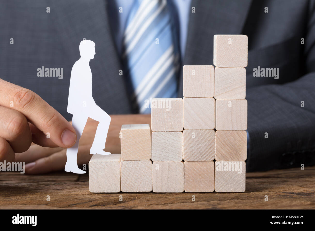 Closeup of businessman moving paper man upstairs made of wooden blocks on table Stock Photo