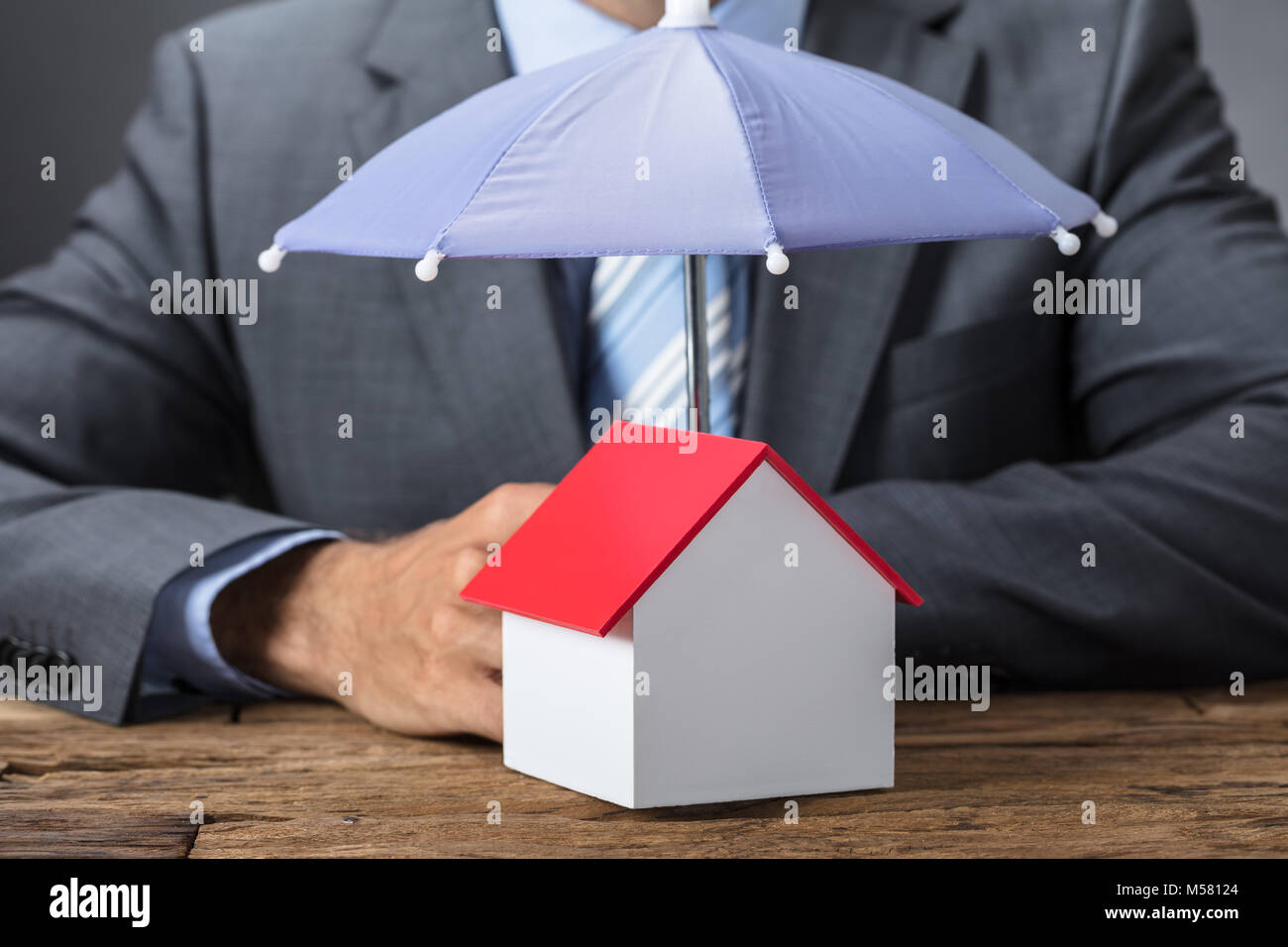 Closeup of businessman protecting house model with umbrella at table Stock Photo
