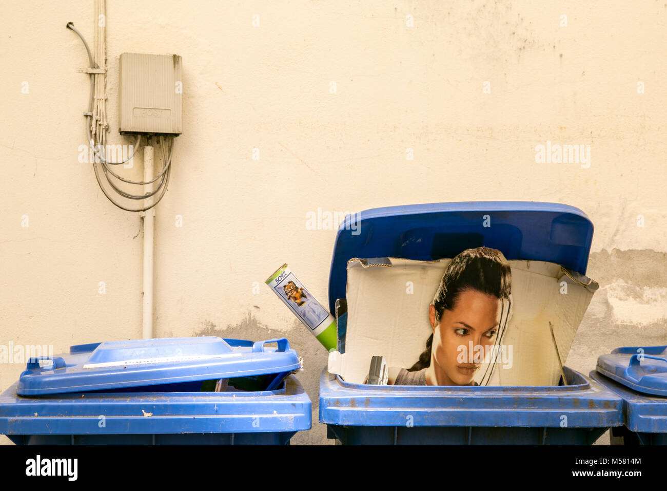 An Angelina Jolie Tomb Raider stand-up display littered into a blue grabage bin. Stock Photo