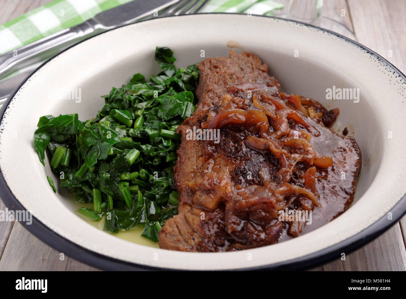 Beef steak with onion and spinach on a rustic table Stock Photo