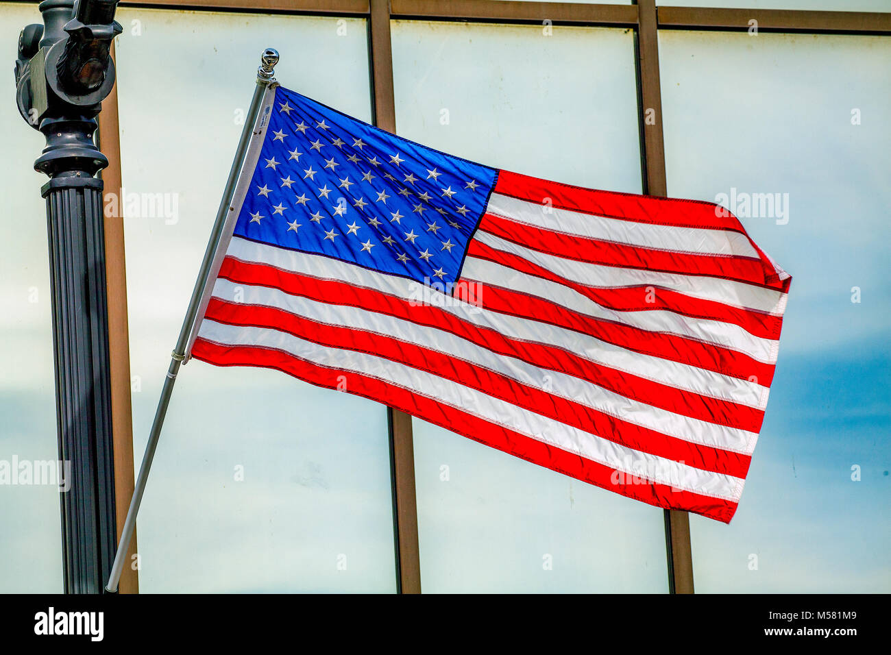 A bright, colorful American flag attached to a black, iron pole waves in the breeze outside a bank window in Littleton, NH, USA. Stock Photo