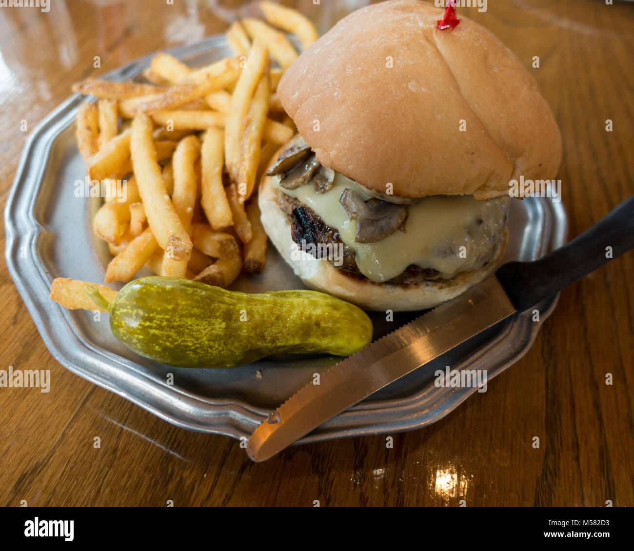 A mushroom and Swiss cheeseburger with French fries (chips) and a dill pickle served at Raindancer Restaurant in Amsterdam, NY USA Stock Photo