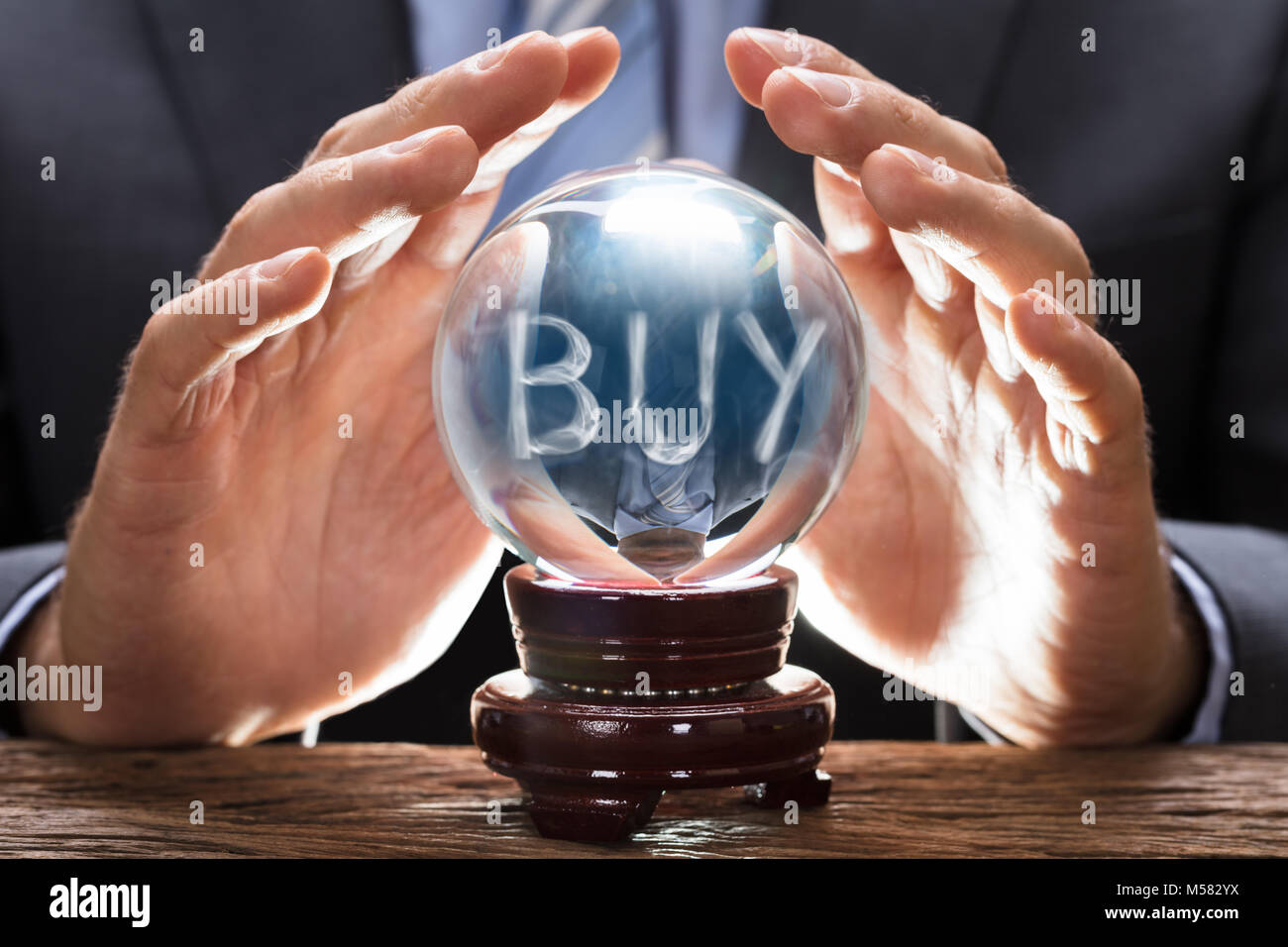 Midsection of businessman covering crystal ball with smoke forming buy text at wooden table Stock Photo
