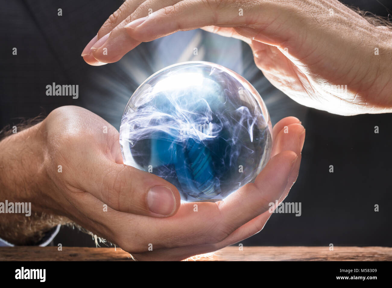 Midsection of businessman covering crystal ball with swirling smoke at wooden table Stock Photo