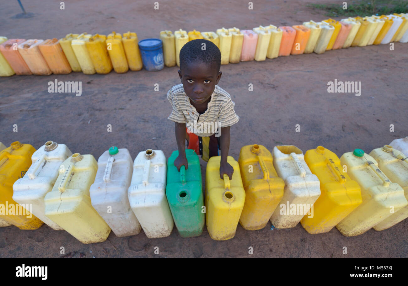 A boy from South Sudan keeps watch on a row of jerry cans before dawn in the Rhino Refugee Camp in northern Uganda. Stock Photo