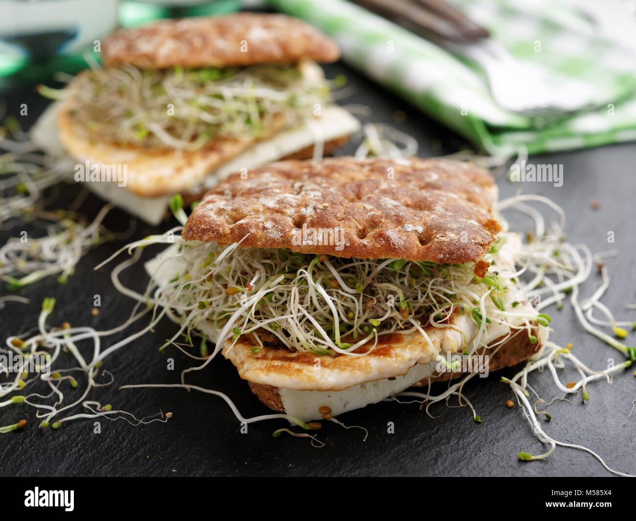 Two sandwiches with grilled turkey meat, slice of cheese, and radish sprouts on a slate cutting board Stock Photo