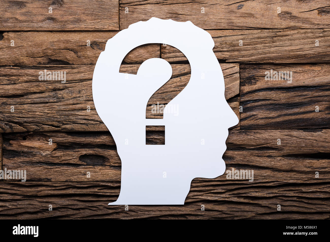 Directly above shot of paper businessman's head with question mark on wooden table Stock Photo