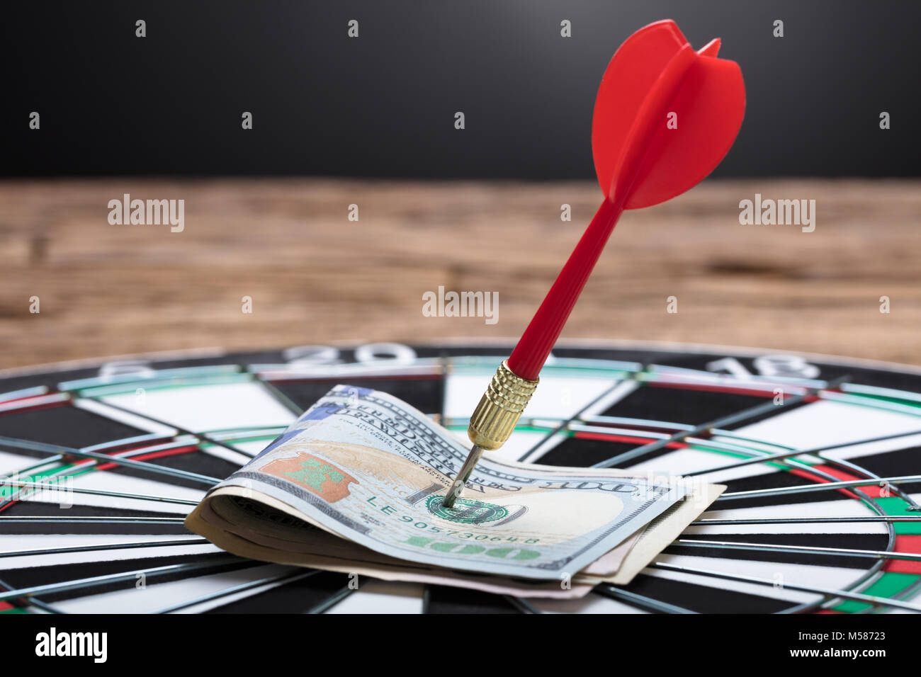 Closeup of arrow in papernotes on dartboard at table against black background Stock Photo