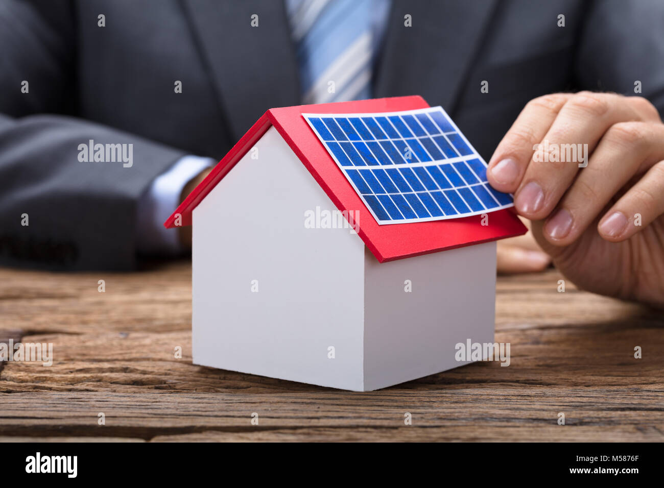 Midsection of businessman sticking solar panel on model home at wooden table Stock Photo
