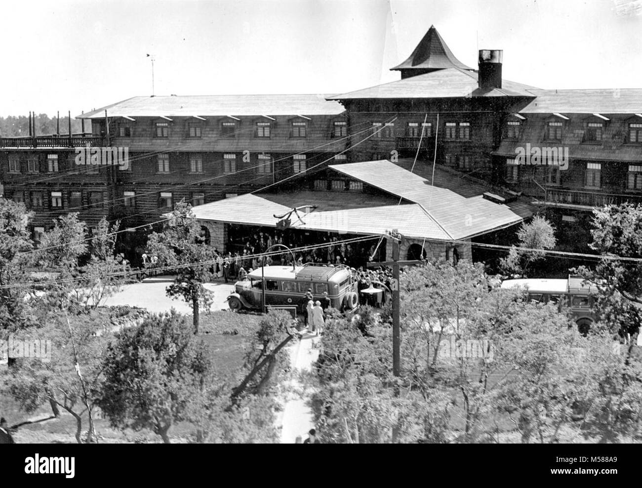 Grand Canyon Historic El Tovar Hotel. TELEPHOTO VIEW OF THE FRONT ENTRANCE TO EL TOVAR HOTEL (FROM THE ROOF OF HOPI HOUSE) HARVEYCAR TOUR BUSSES PARKED IN FRONT. LARGE SHRINER GROUP ON PORCH. CIRCA 1931. FRED HARVEY PHOTO. Historic photo from , Stock Photo