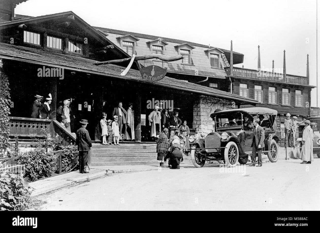 A Grand Canyon Historic El Tovar Hotel. VISITORS STANDING AROUND THE FRONT ENTRANCE  TO THE EL TOVAR HOTEL. HOPI DEMONSTRATORS POSING. TOUR AUTOMOBILE. CIRCA 1922. FRED HARVEY PHOTO. Historic photo from , Stock Photo