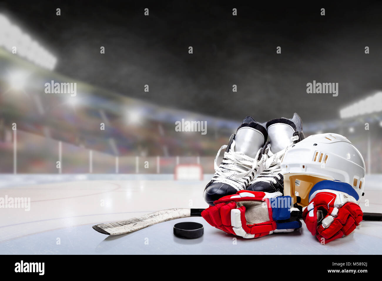 Ice hockey helmet, skates, gloves, stick and puck in brightly lit outdoor stadium with focus on foreground and shallow depth of field on background. D Stock Photo