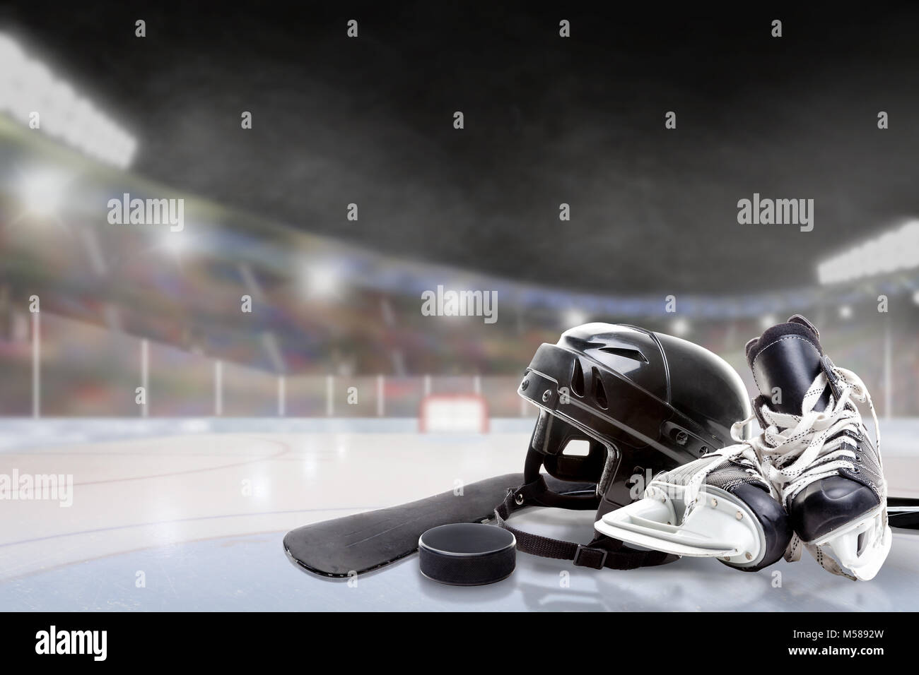 Ice hockey helmet, skates, stick and puck in brightly lit outdoor stadium with focus on foreground and shallow depth of field on background. Deliberat Stock Photo