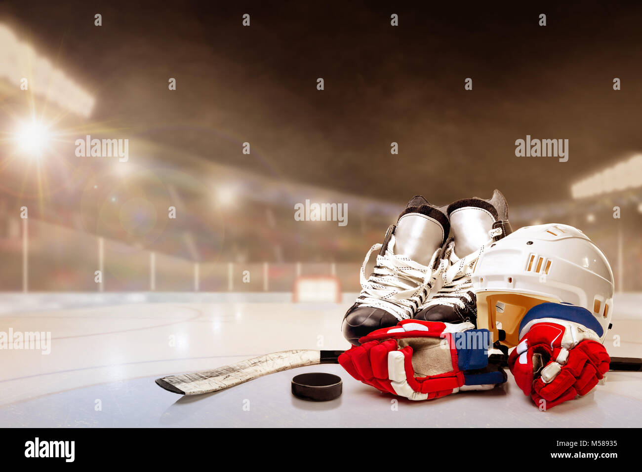 Ice hockey helmet, skates, gloves, stick and puck in brightly lit outdoor stadium with focus on foreground and shallow depth of field on background. D Stock Photo