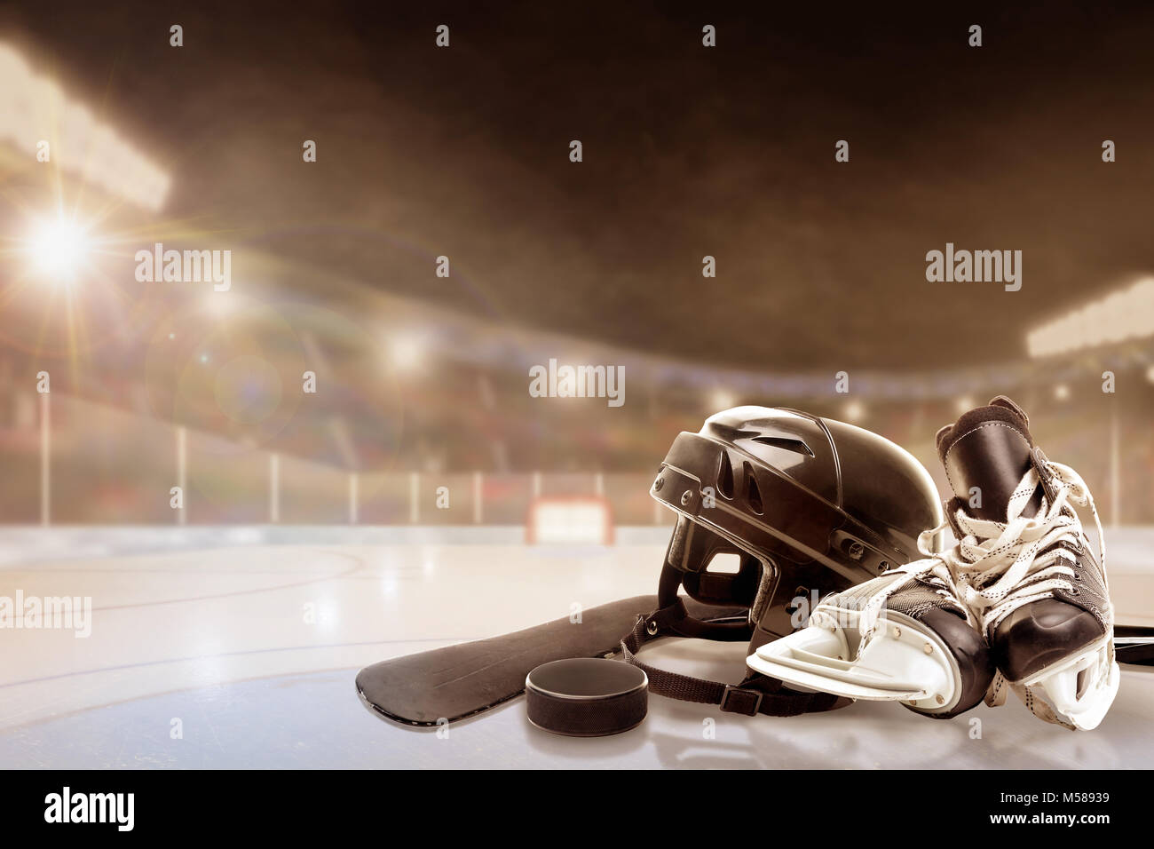 Ice hockey helmet, skates, stick and puck in brightly lit outdoor stadium with focus on foreground and shallow depth of field on background. Deliberat Stock Photo