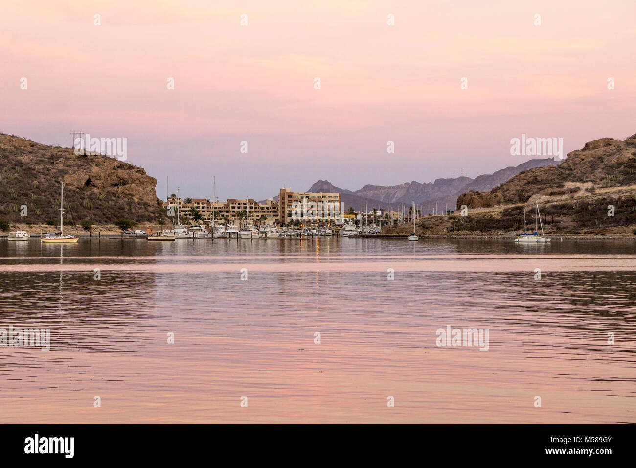 lovely rose tinted twilight sky reflected in calm water of San Carlos bay with San Carlos Marina boats hotel shops in distance across glowing bay Stock Photo
