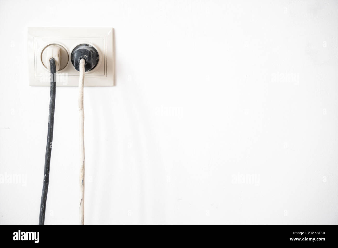 Electric socket with two stuck electric plugs on a white wall. Power