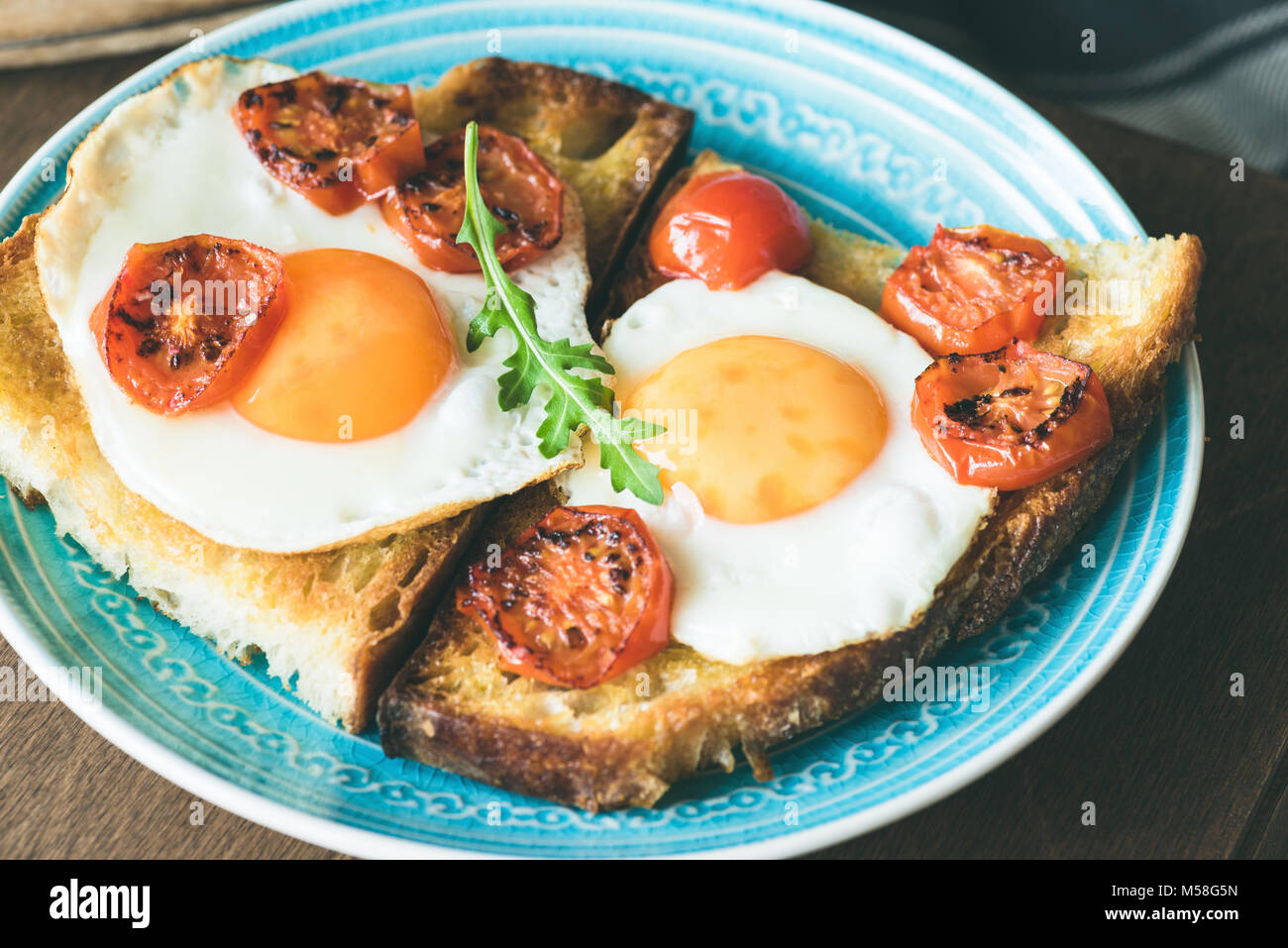 Breakfast toast with egg, roasted tomatoes and arugula salad on blue