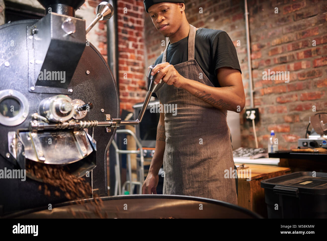 Black worker busy pulling the lever that pours the coffee beans from the roaster over to a drying tray where they will cool down before being packaged Stock Photo