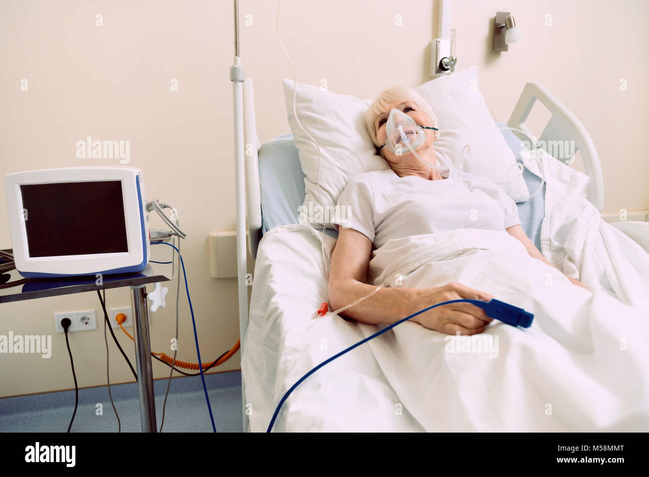 Retired lady lying in hospital bed with respiratory support Stock Photo