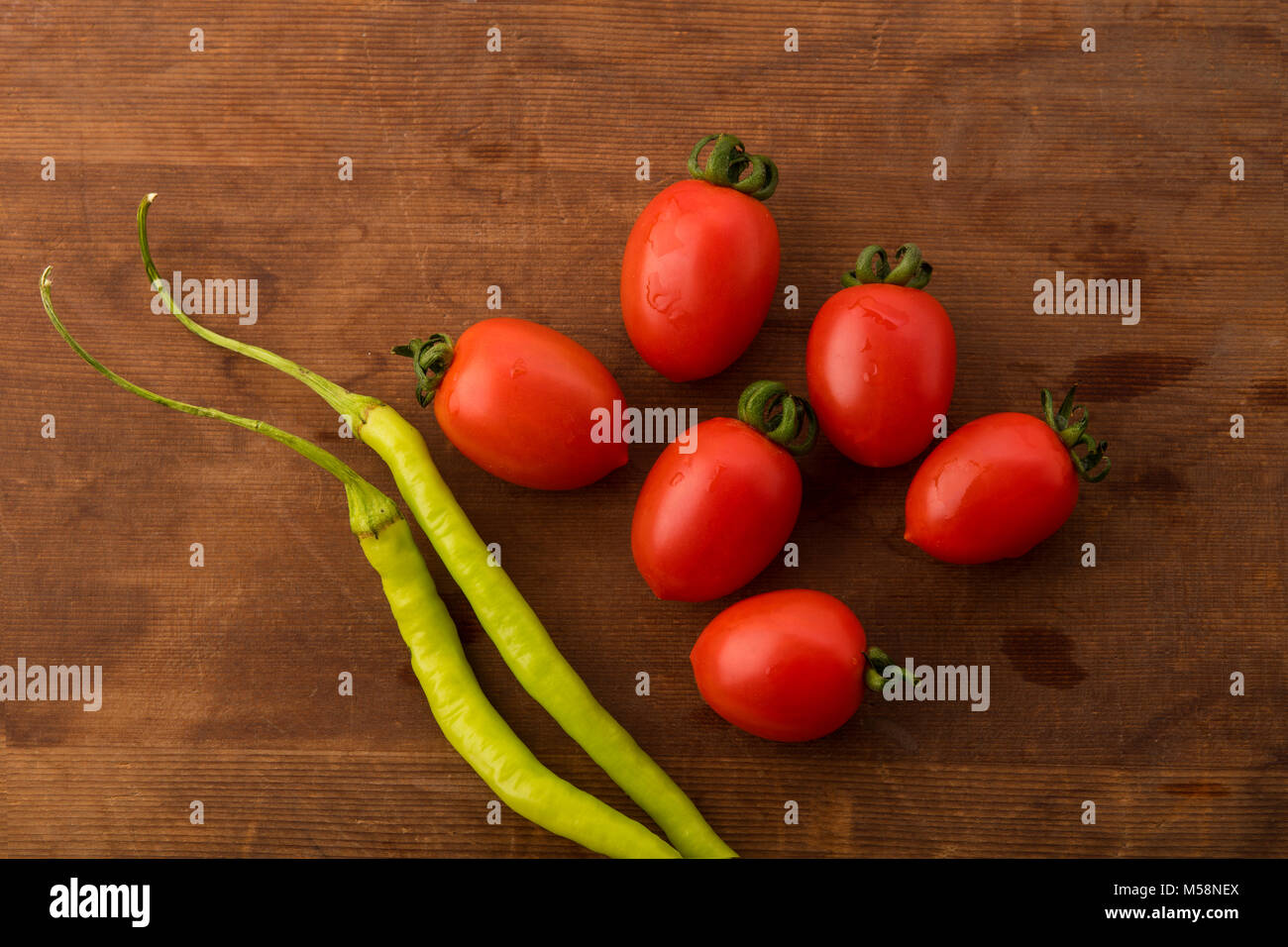 Vegetable: Top View of Fresh Red Baby Tomatoes and Green Chilies on Brown Wooden Background Stock Photo