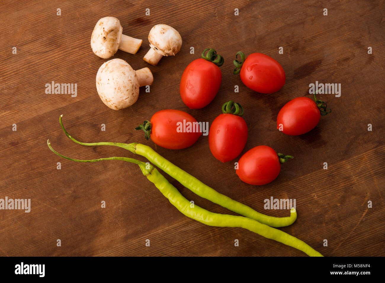 Vegetable: Top View of Fresh Red Baby Tomatoes , Button Mushrooms and Green Chilies on Brown Wooden Background Stock Photo