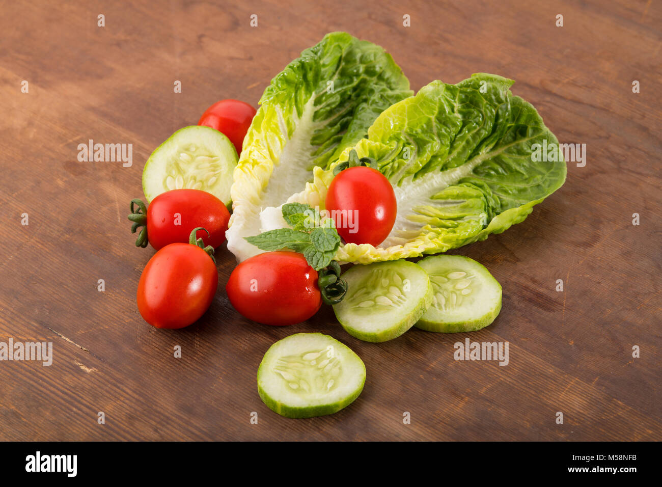 Vegetable: Fresh Green Romaine Lettuce with Baby Tomatoes, Mint Leaves and Cucumber Slices on Brown Wooden Background Stock Photo