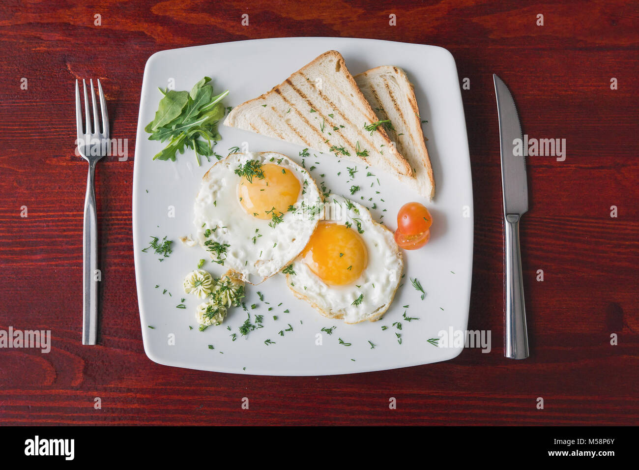 Fried eggs on white plate with green and tomato cherry - breakfast, top view Stock Photo