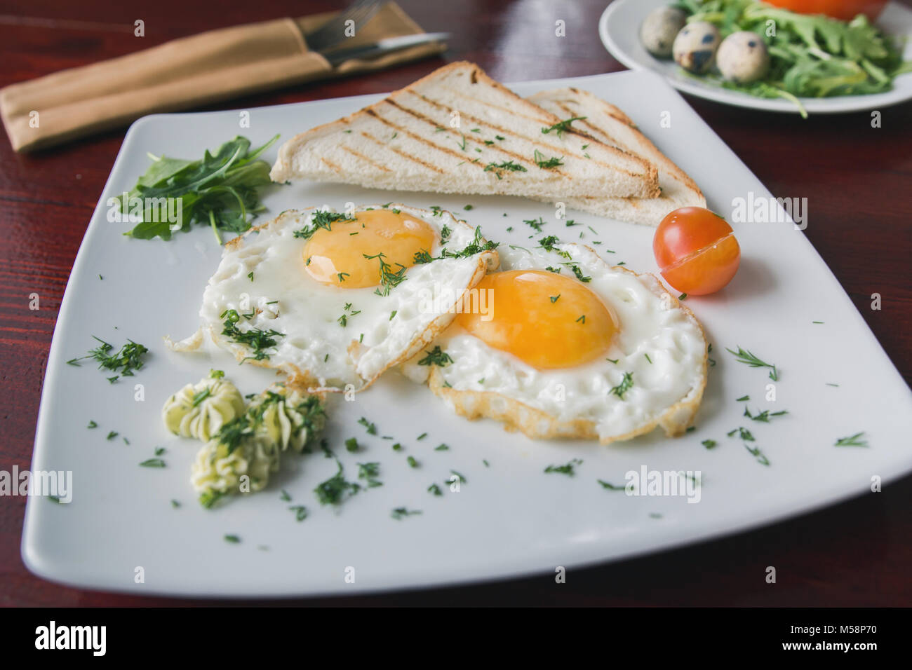 Fried eggs on white plate with green and tomato cherry - breakfast Stock Photo