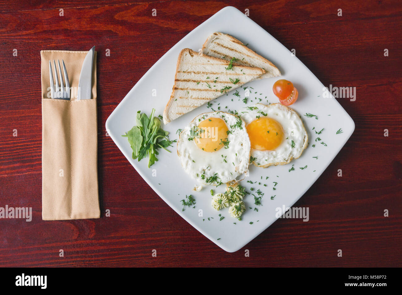 Breakfast in restaurant - fried eggs on white plate with green and tomato cherry Stock Photo