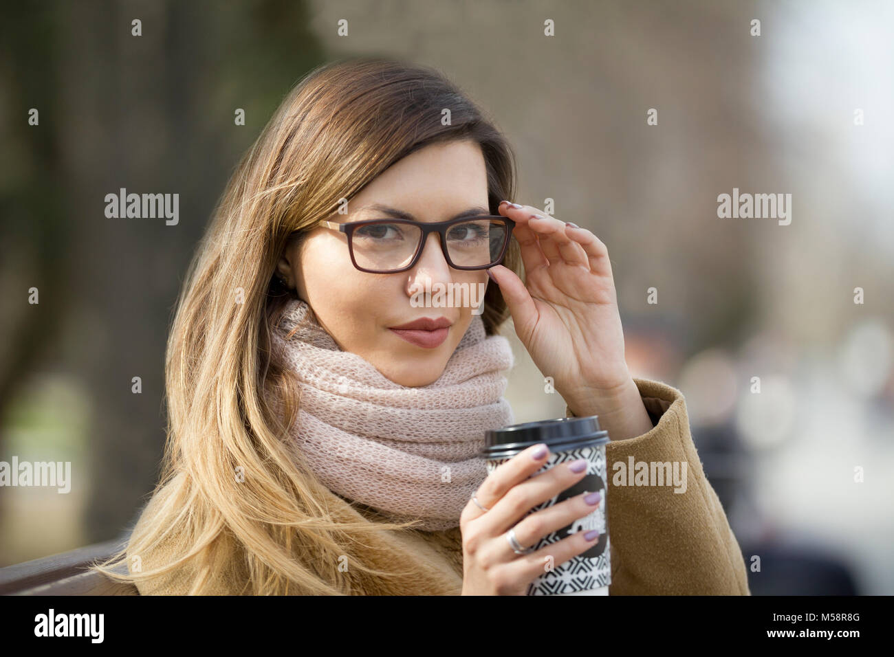 Portrait of young woman in glasses at park drinking coffee Stock Photo