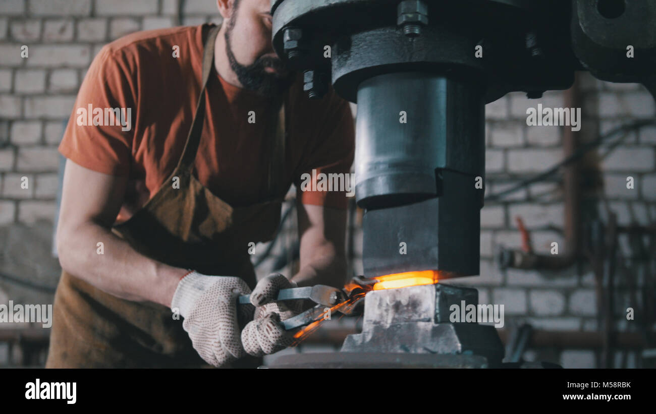 of a blacksmith. A man puts a piece under an automatic