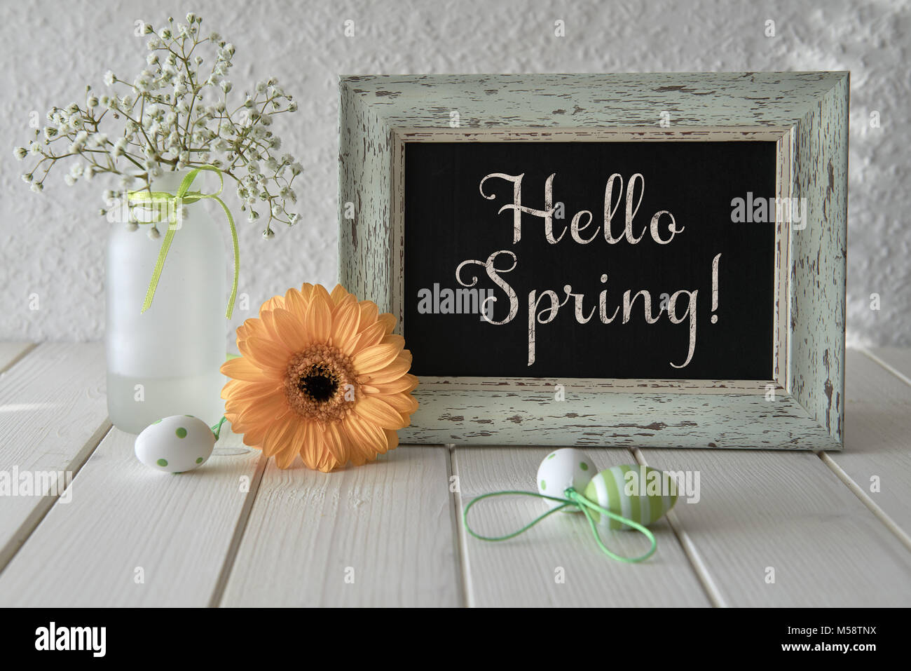 Spring flowers, Easter decorations and a blackboard on white table. Text 'Hello Spring' on a blackboard. Stock Photo
