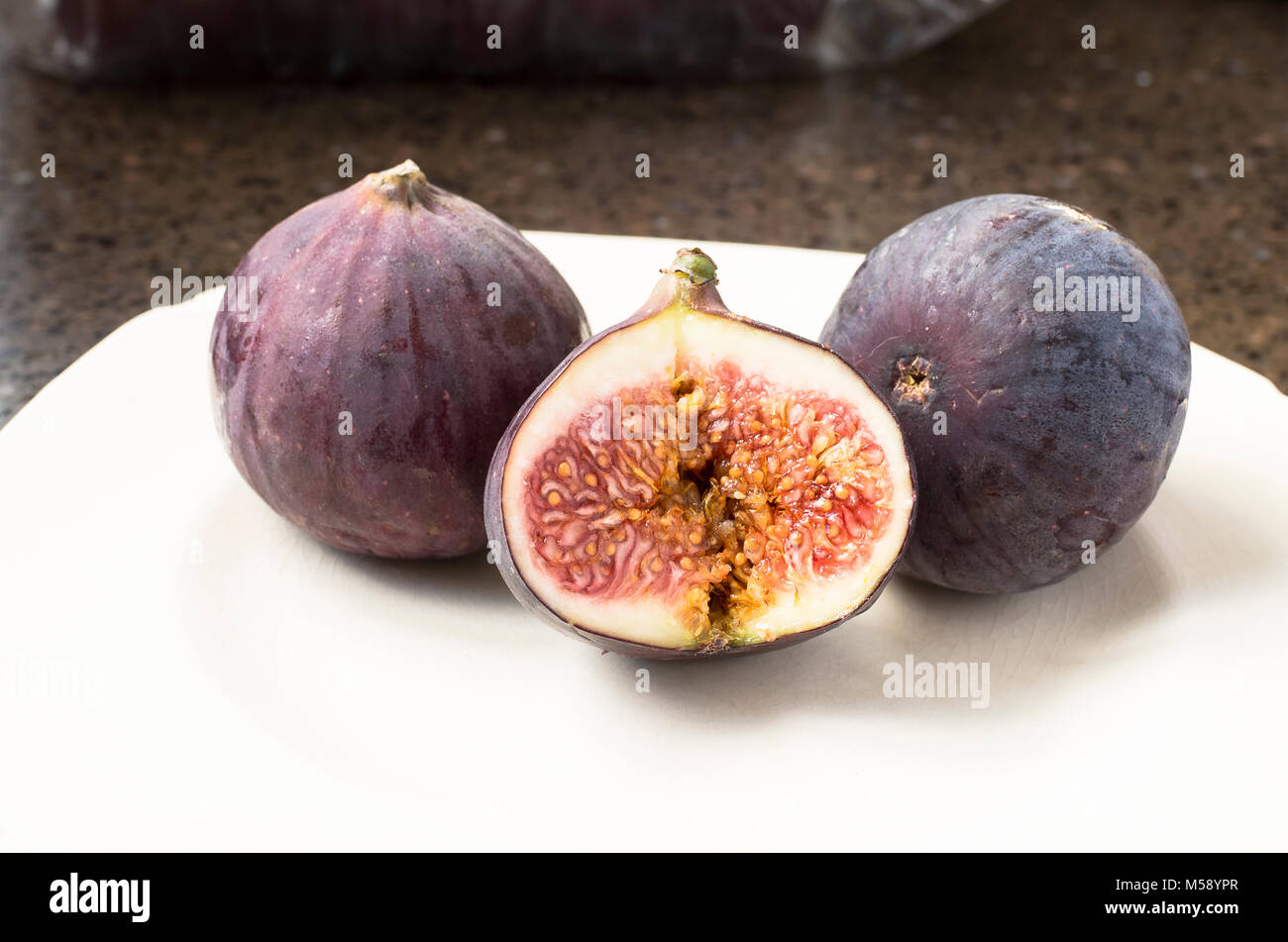 Three fresh Black Bursa ripe figs, one halved to show inside flesh and seeds Stock Photo Alamy
