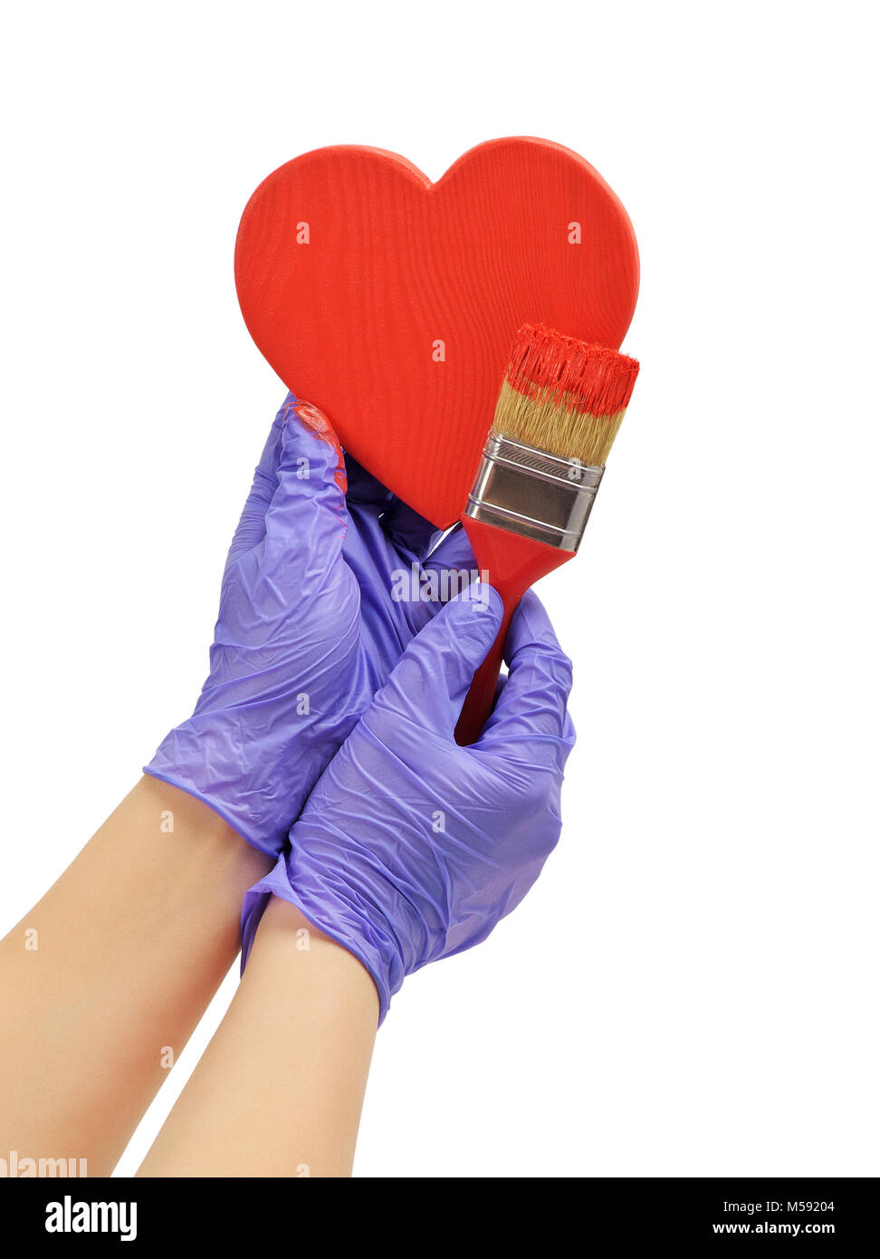hand paints the heart with a brush hand paint in red wooden heart hand in blue glove holds a red brush Stock Photo
