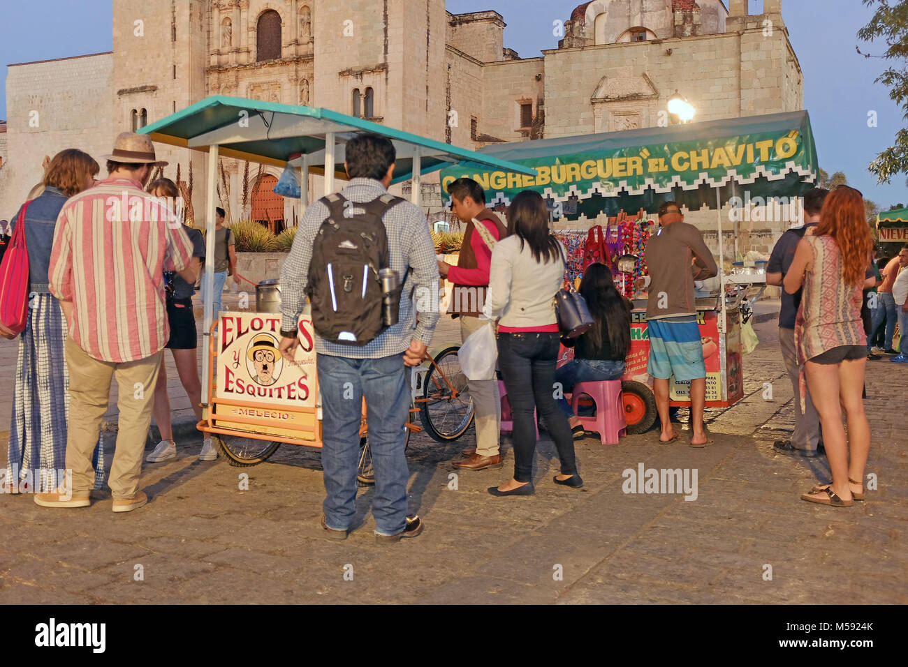 Backpacker travelers congregate around a food stand located in front of the Templo de Santo Domingo in the heart of Oaxaca, Mexico. Stock Photo