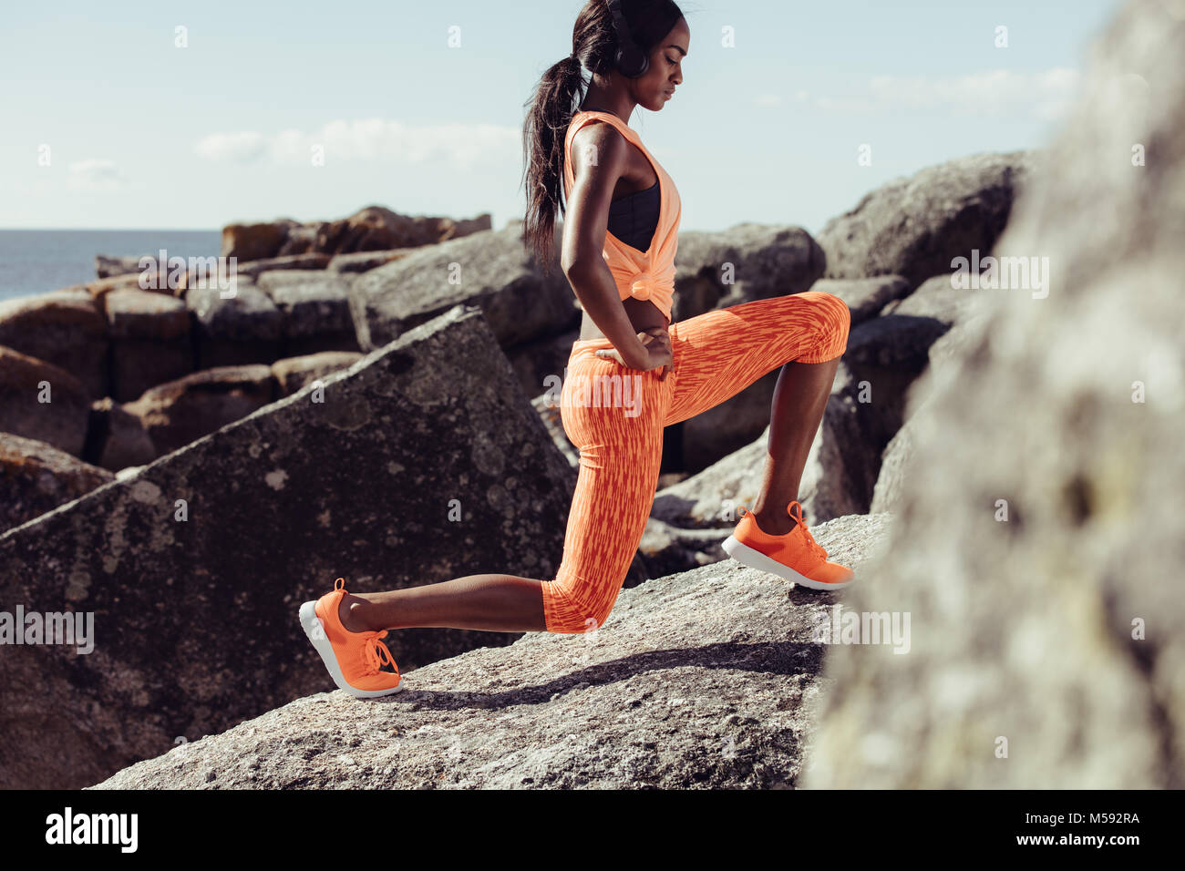 Woman doing warming up exercises on the rocks at the beach. Female athlete stretching her body. Stock Photo