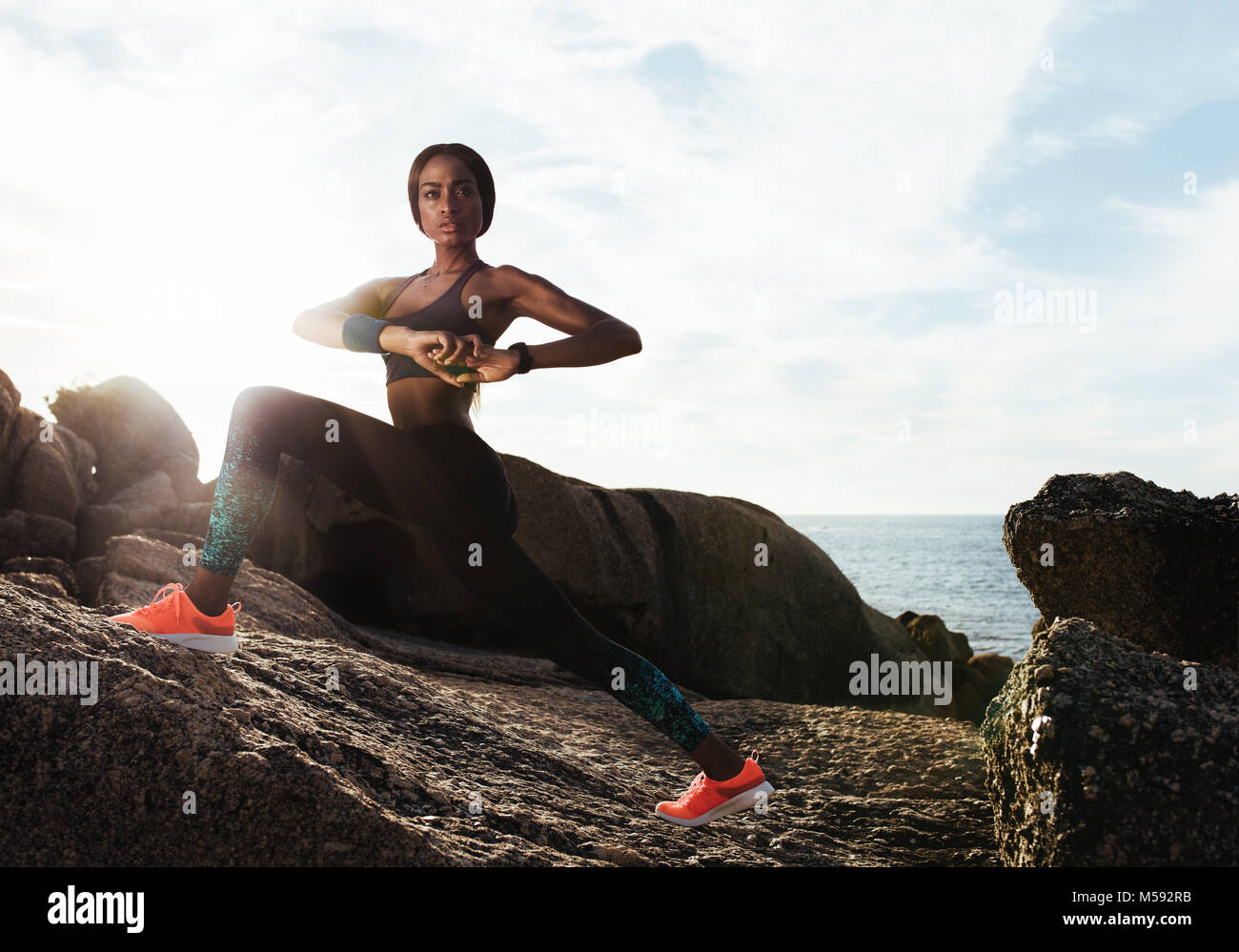 Fit young female runner doing stretches. Young woman stretching outdoors on rocks at beach. Stock Photo