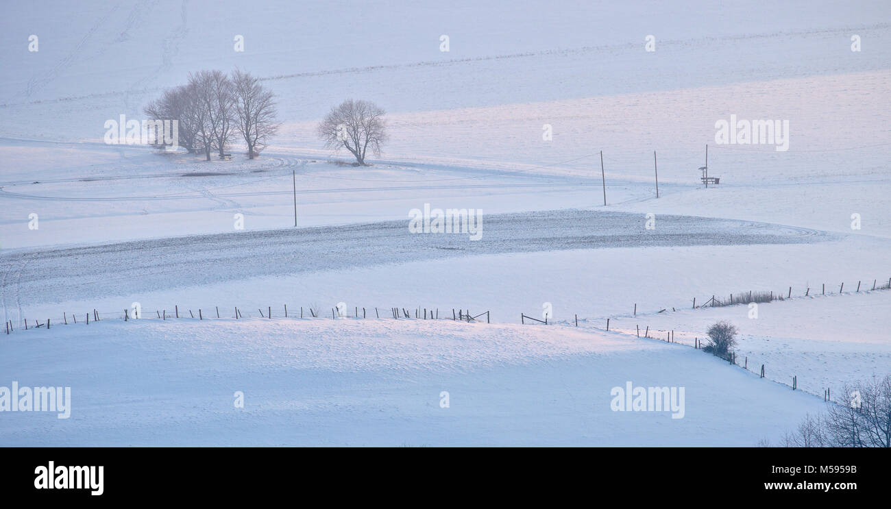 Winter sunset over snowy fields with distant trees and fences (telephoto shot) Stock Photo