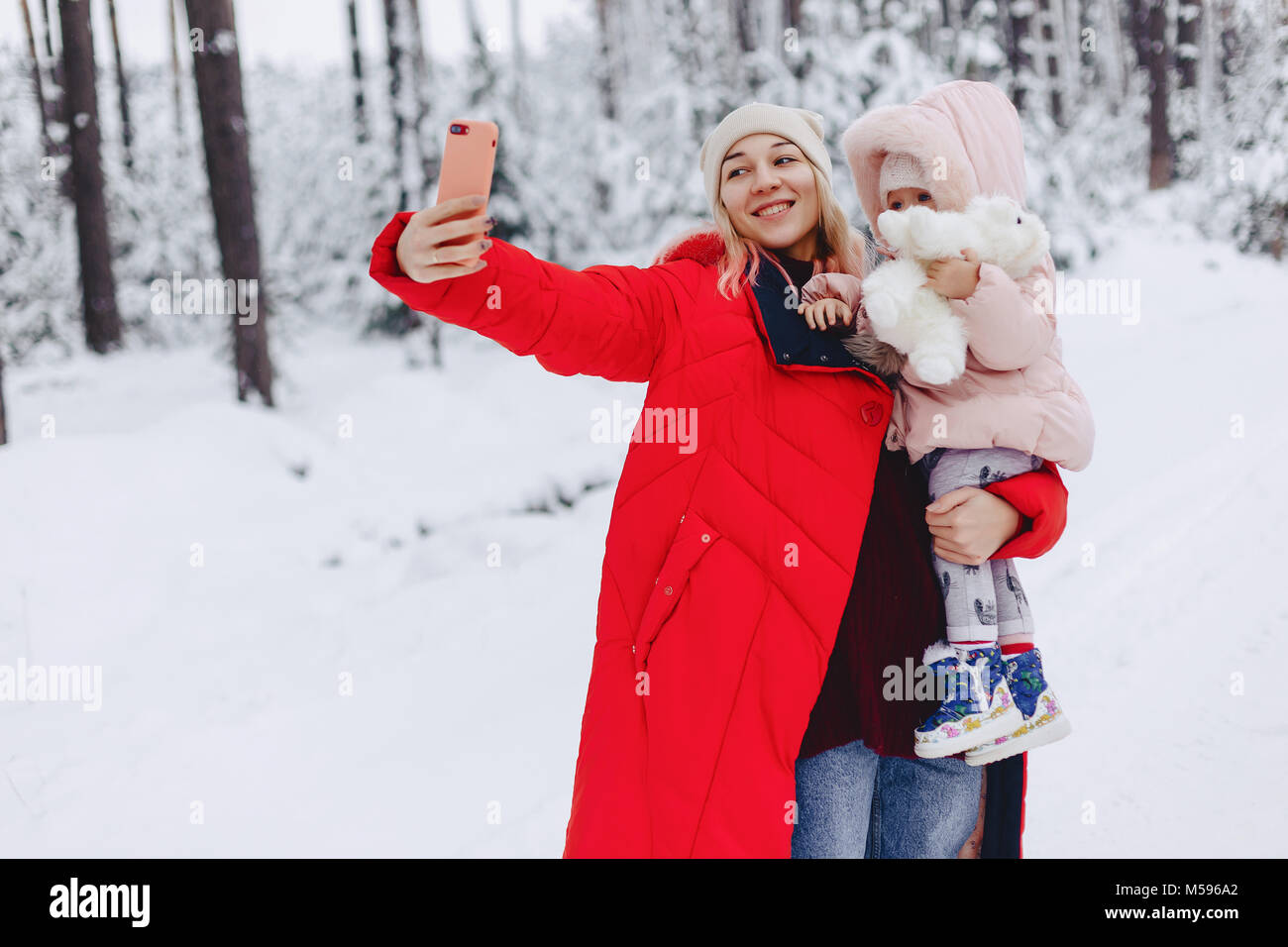 the mom holds a small daughter doing a selfie in the snowy picturesque area of the pine forest on the highway Stock Photo