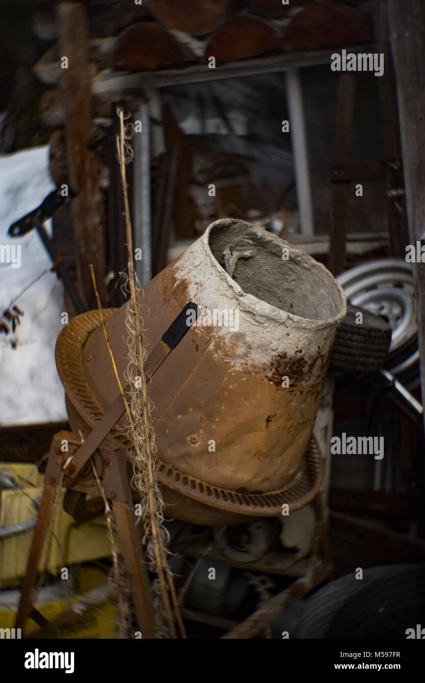An old, rusty electric cement mixer in from of an abandoned cabin in the woods, on Eagle View, in the Cabinet Mountains, in Sanders County, Montana Sh Stock Photo