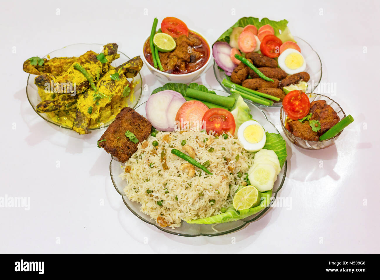 Popular Bengali Indian food dishes with fried rice, fish fingers, mutton masala curry and tangra fish curry garnished with salad. Stock Photo