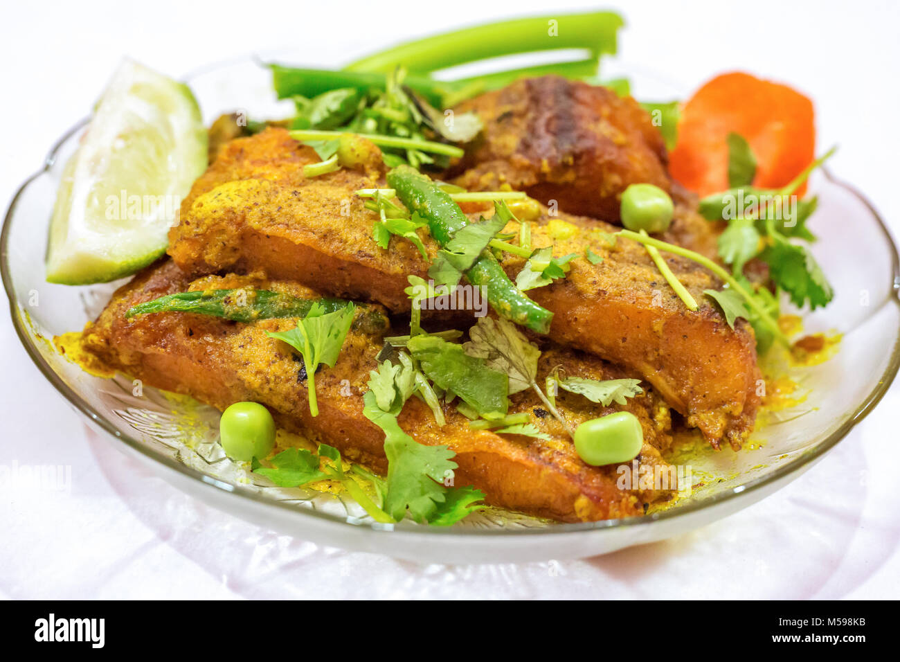 Spicy rohu fish masala curry garnished with coriander, beans, carrot, green chili and lemon slice. Rohu fish is a popular non vegetarian diet in India. Stock Photo
