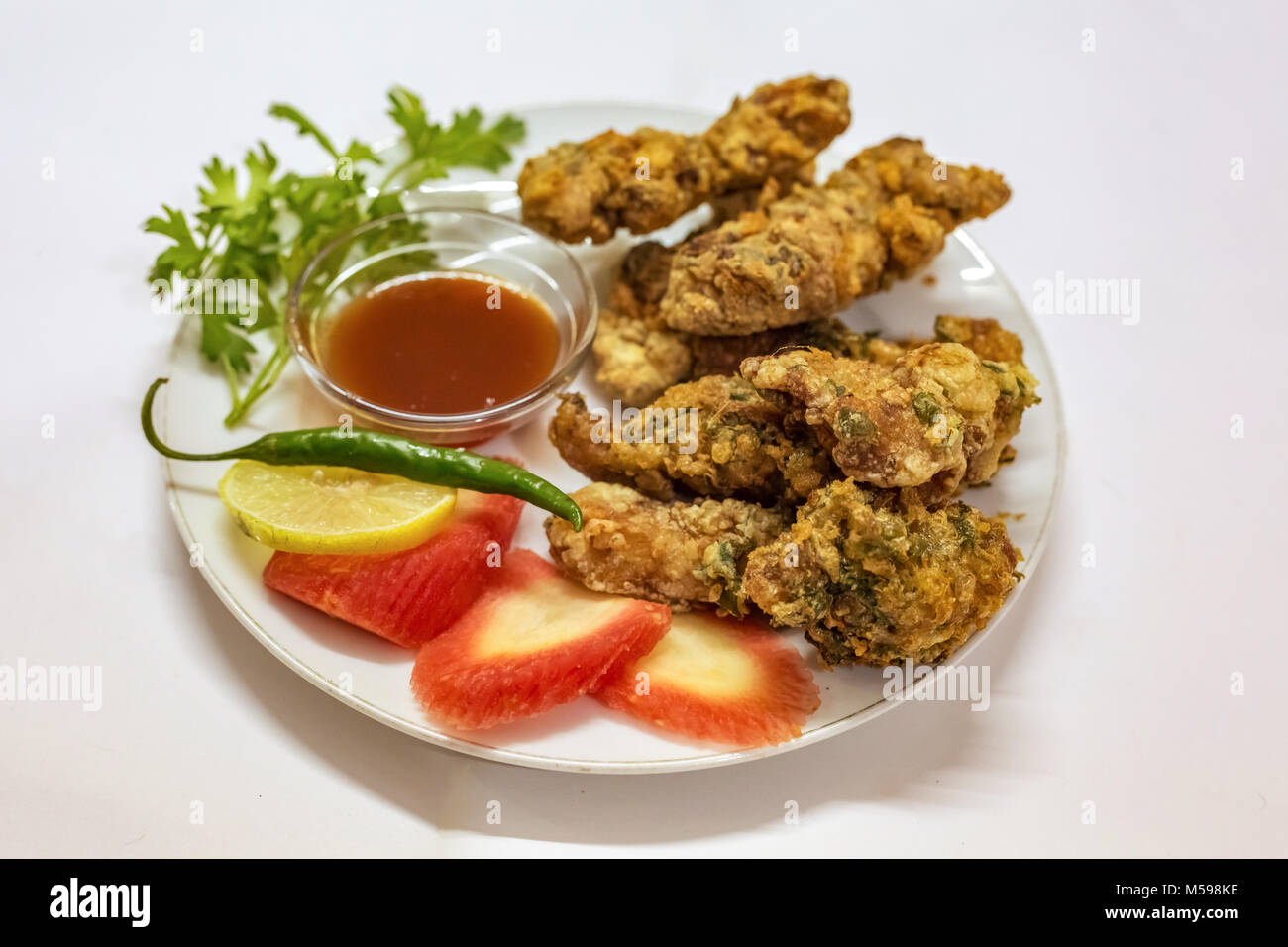 Deep fried spicy chicken pakora served with tomato sauce and sliced carrot lemon with coriander leaf with green chili. A popular Indian starter dish. Stock Photo