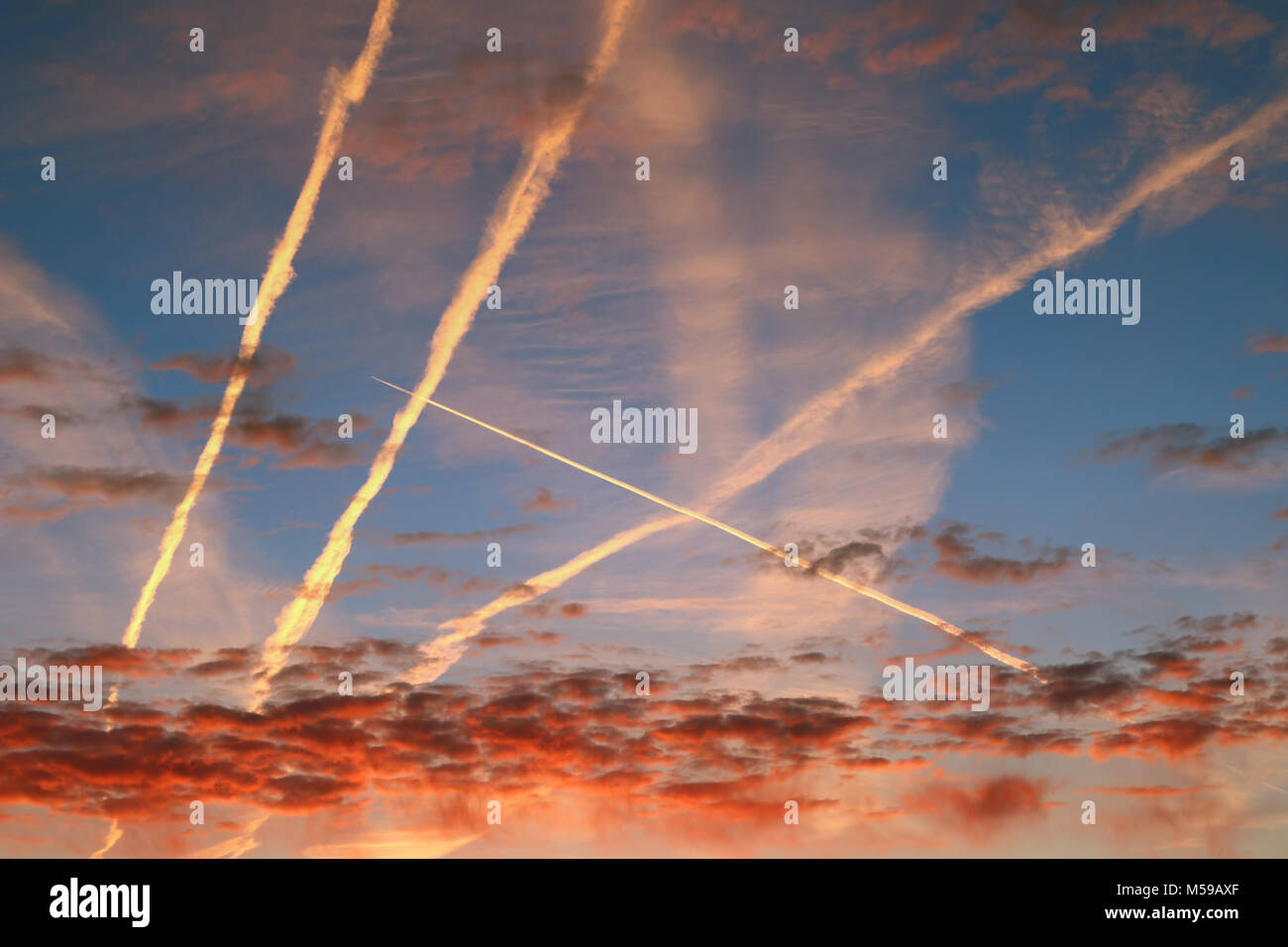 Red morning clouds and streams of condensed vapor on the sky Stock Photo