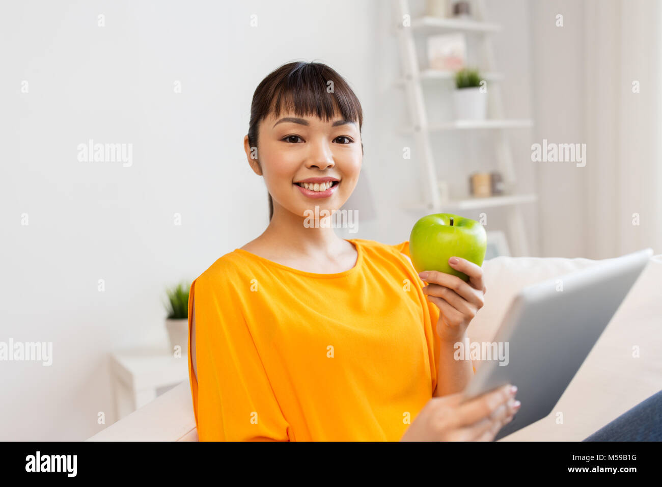 happy asian woman with tablet pc and apple at home Stock Photo - Alamy